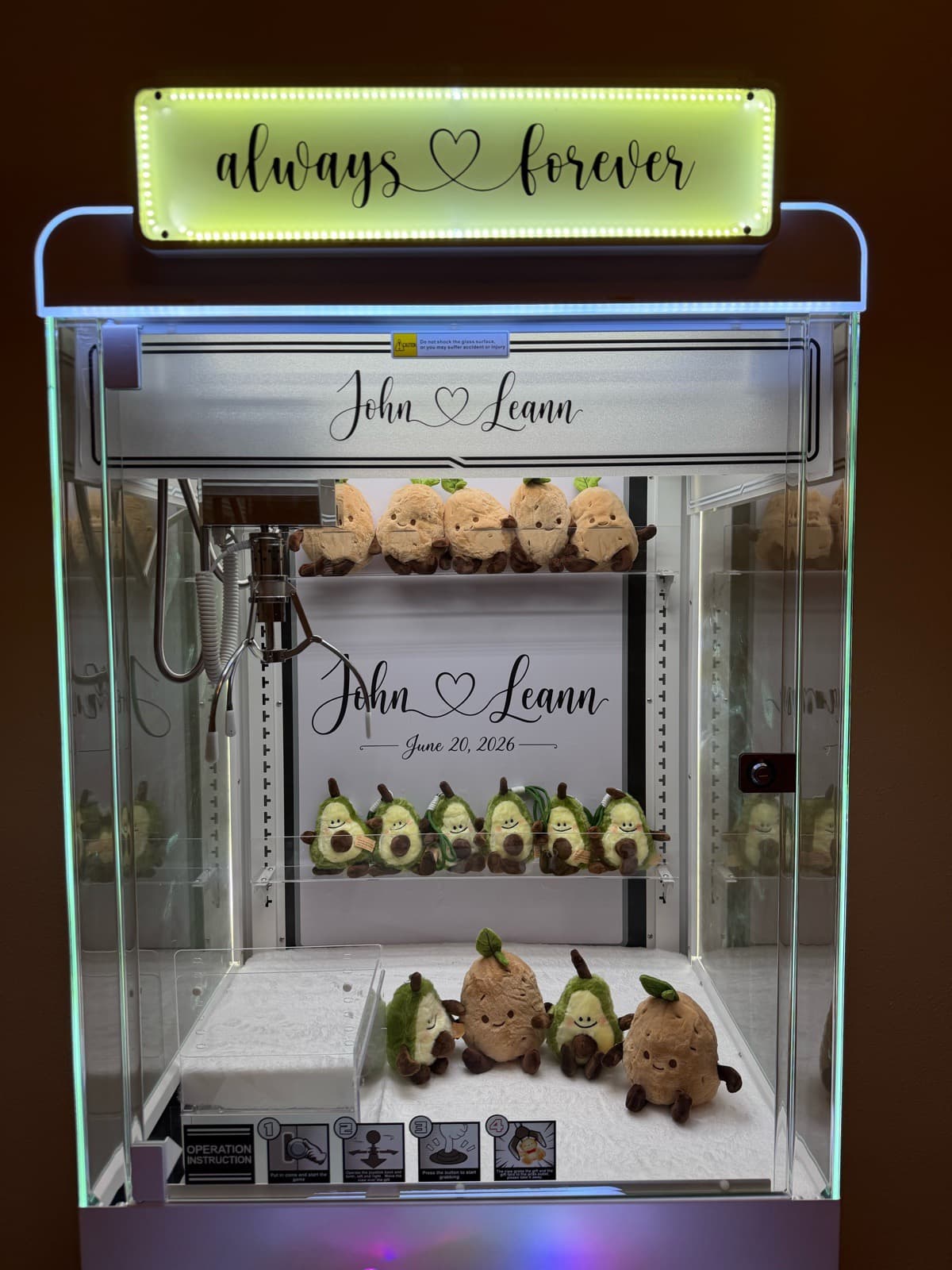 Front view of a wedding claw machine with a personalized marquee sign and plushies inside