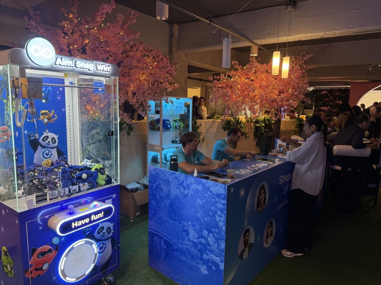 Copado branded claw machine filled with mascot plushies beside the Copado Community booth at Dreamforce 2026