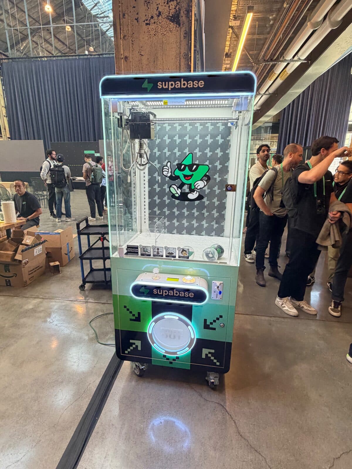 Supabase branded claw machine with lit green marquee, pixel-arrow control panel, and mascot backdrop at the Supabase Select 2026 Hackathon in San Francisco